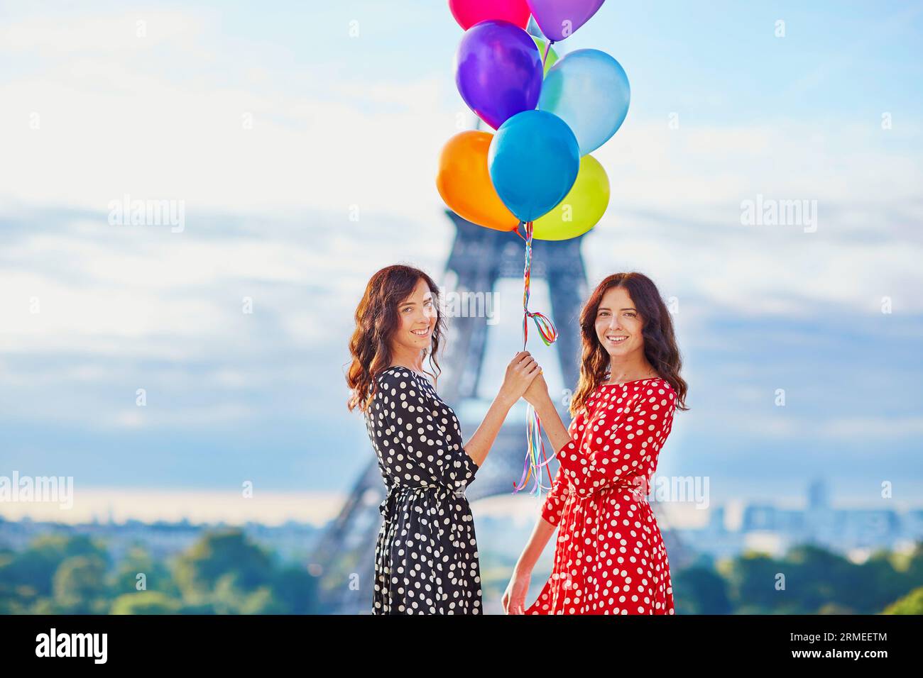 Belles sœurs jumelles dans des robes à pois rouges et noires avec un énorme bouquet de ballons colorés devant la tour Eiffel à Paris, France Banque D'Images