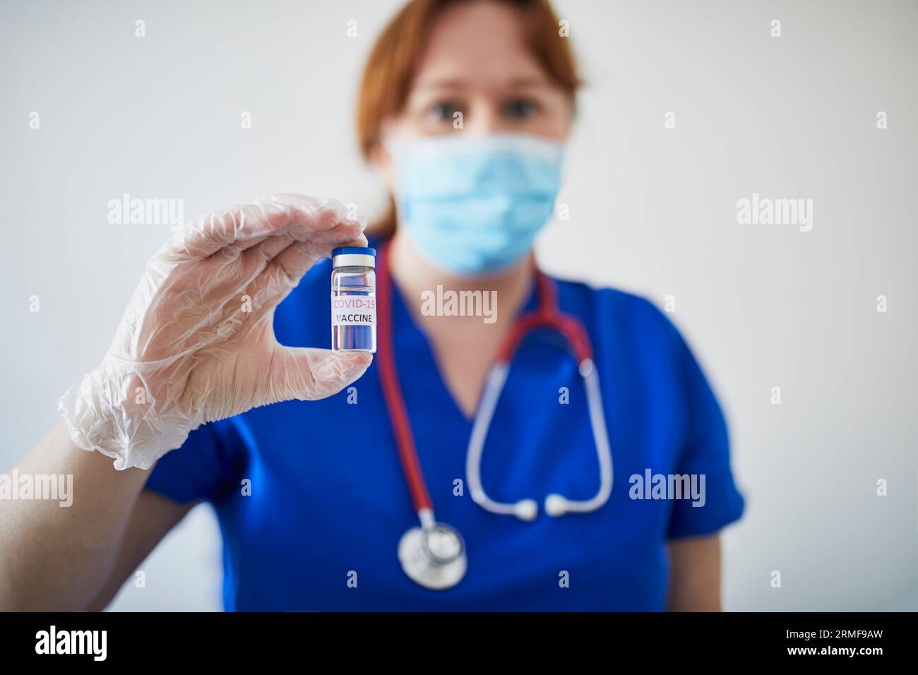 Médecin ou infirmière avec stéthoscope, portant un masque facial et des gants stériles, tenant un flacon contenant le vaccin COVID-19. Recherche, essai clinique, vaccinati Banque D'Images