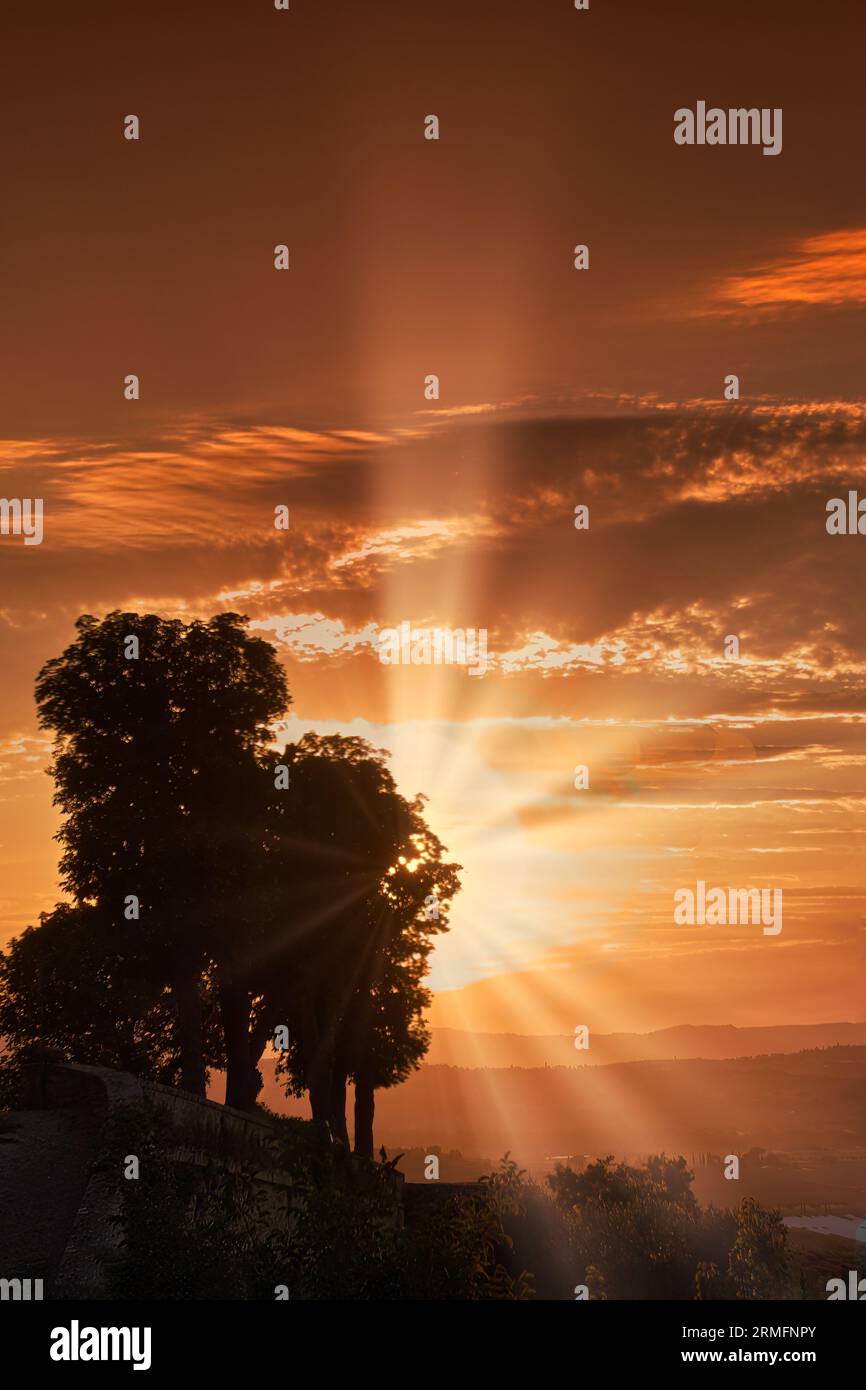 Ombrie, Italie. Collines au sud du lac Trasimeno. Rayons de soleil à travers les nuages au coucher du soleil avec un ciel orange. Banque D'Images