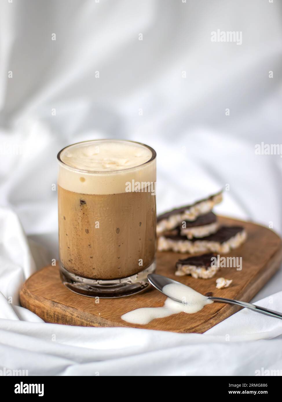 Un gros plan d'un café latte froid fraîchement préparé servi dans un verre sur une planche de bois, posé sur un drap de lit blanc Banque D'Images