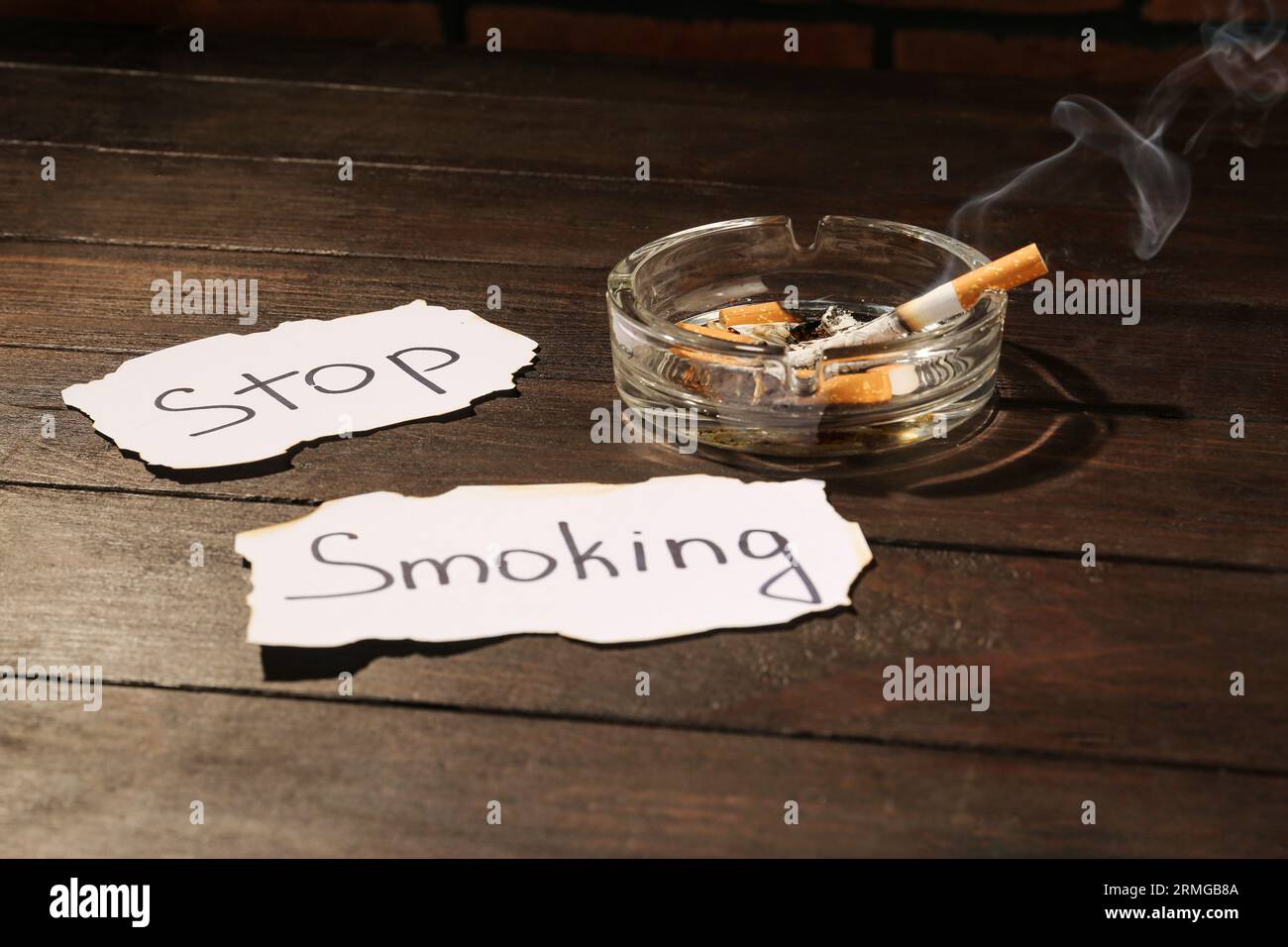 Cendrier avec des cigarettes brûlées et des mots Stop Smoking écrit sur du papier sur une table en bois Banque D'Images