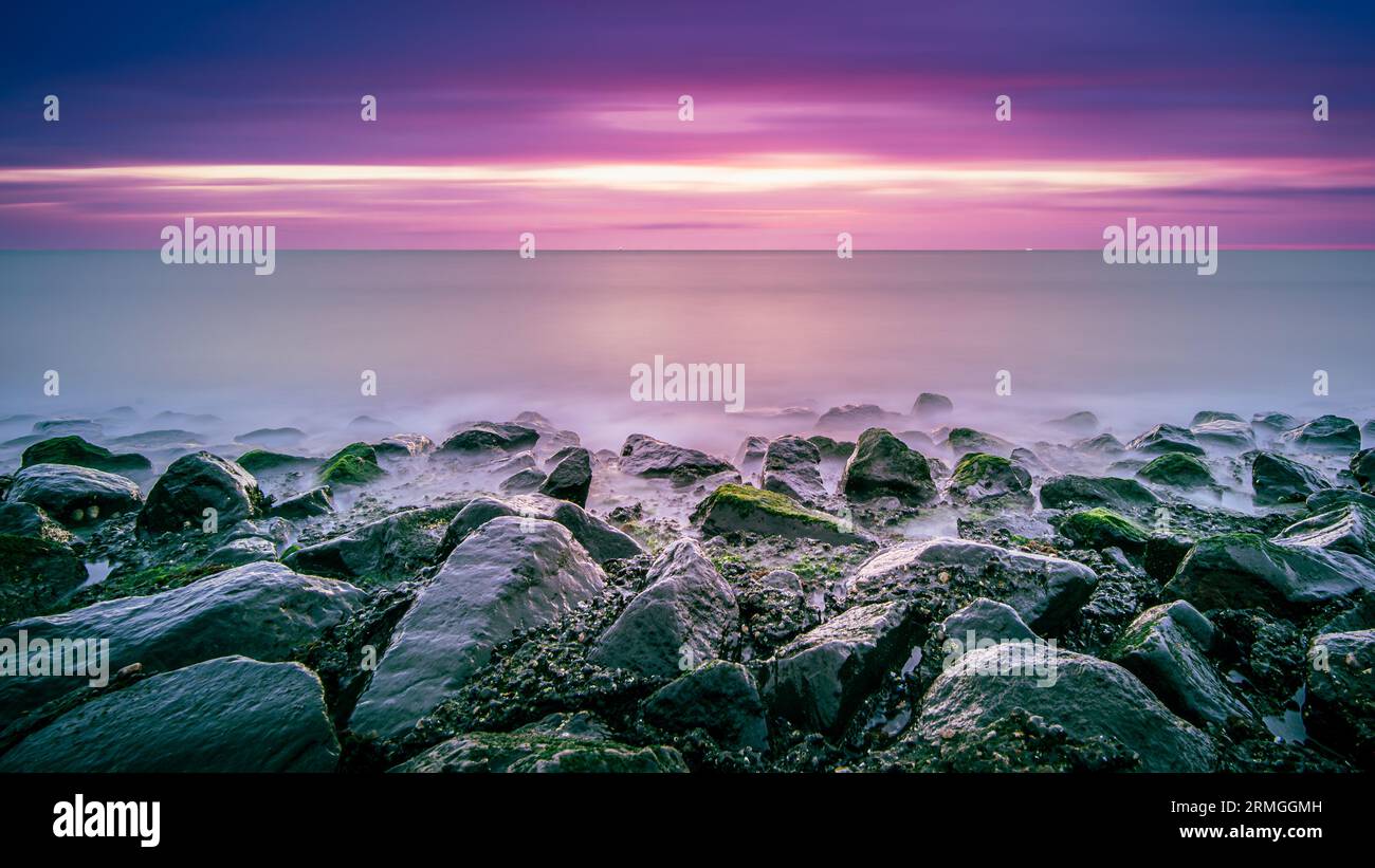 Doux coucher de soleil sur la côte de la mer. Vue imprenable sur les vagues s'écrasant sur les formations rocheuses sous un ciel pastel à West Kapelle, Zeeland, pays-Bas Banque D'Images