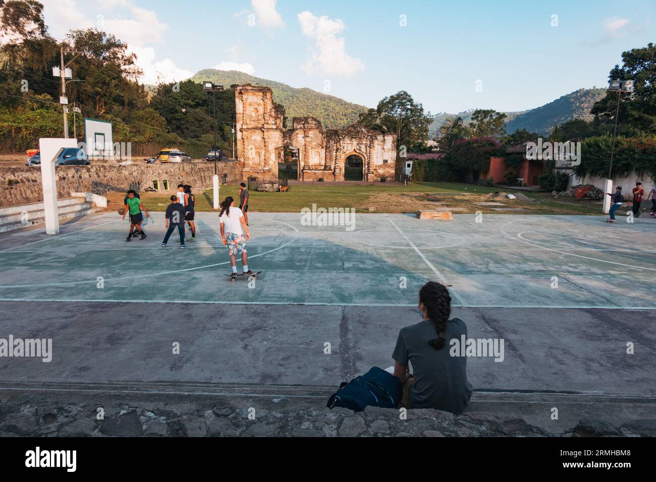 Une femme regarde des enfants jouer au basket-ball sur un court public, avec les ruines d'un bâtiment colonial espagnol reposant derrière, à Antigua Guatemala Banque D'Images