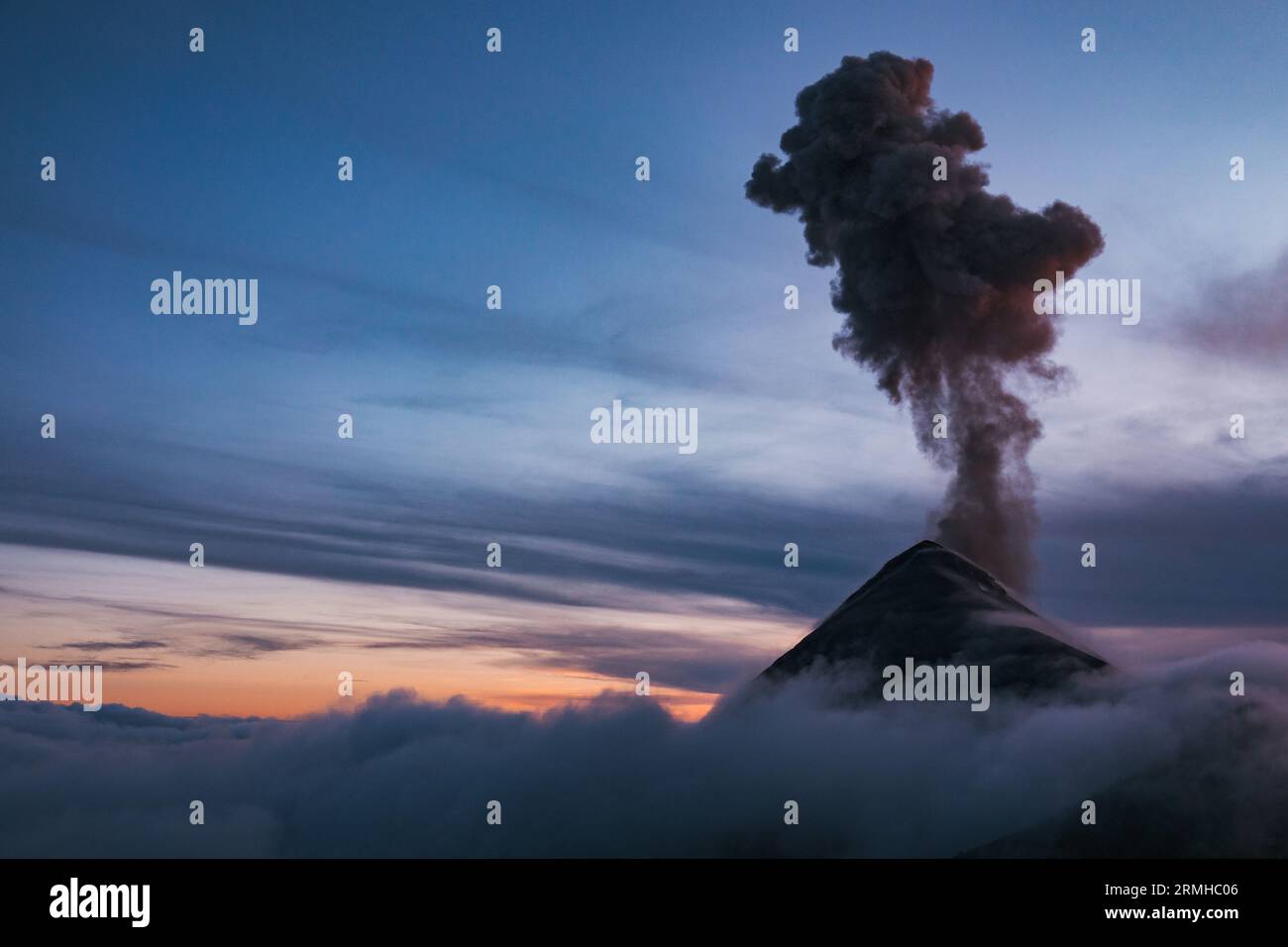 Une scène dramatique comme le volcan Fuego au Guatemala entre en éruption à travers les nuages bas du soir, envoyant un panache sombre de cendres haut dans l'air Banque D'Images
