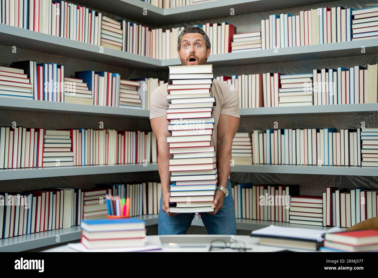 Portrait de professeur drôle avec livre dans la salle de classe de la bibliothèque. Beau professeur dans la bibliothèque universitaire. Professeur drôle tenir beaucoup de livres. Professeur fou avec Banque D'Images