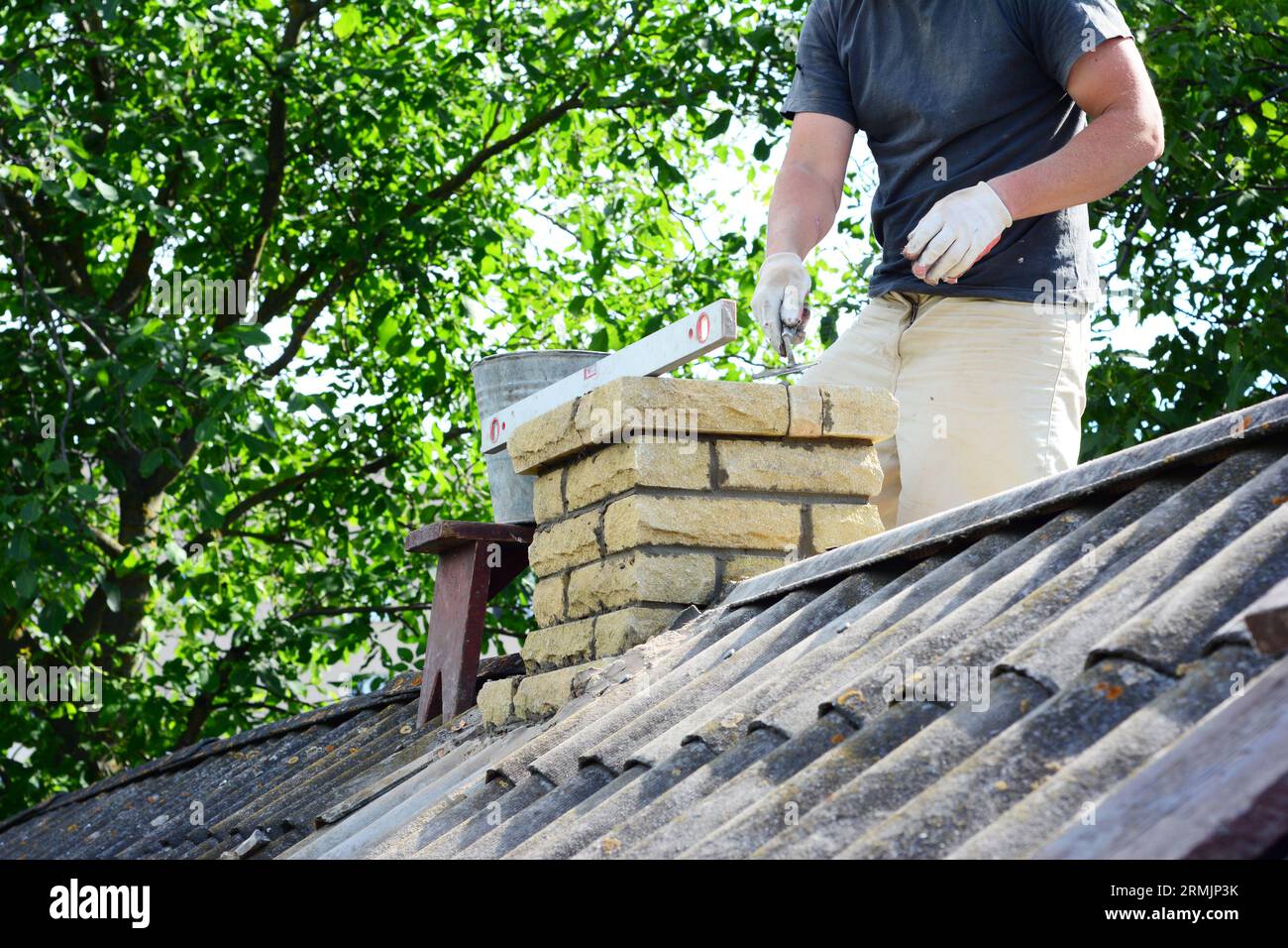 Construction de cheminées, réparations et reconstruction. Un entrepreneur pose en briques une cheminée en brique sur le toit d'une maison en amiante. Banque D'Images