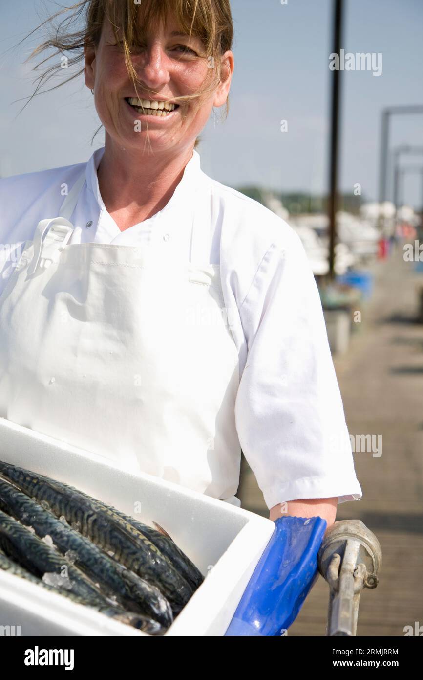 Portrait of smiling poissonnier tenant un récipient plein de poisson blanc Banque D'Images