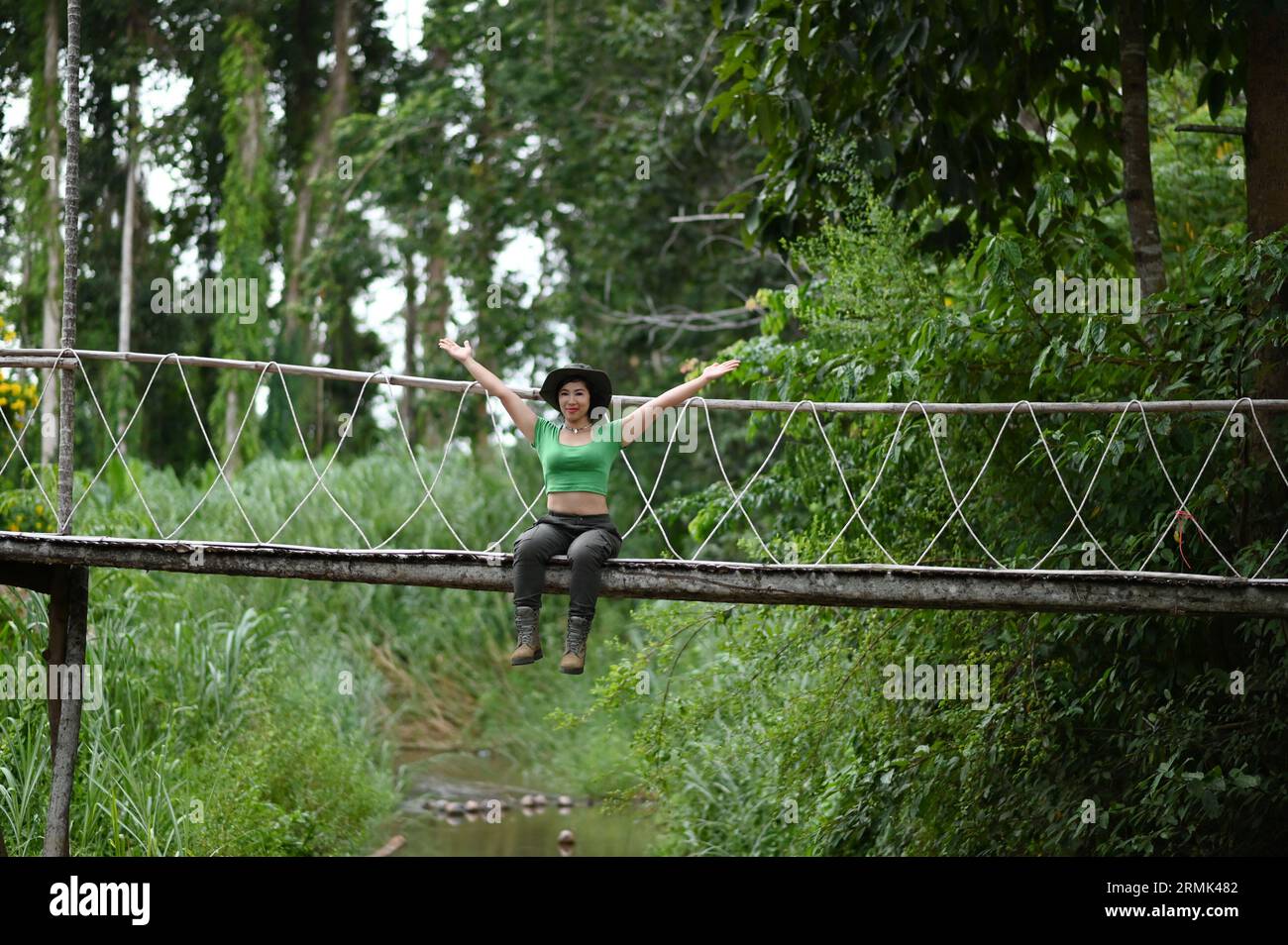 Jolie femme asiatique assise et posant au pont suspendu au-dessus du ruisseau dans la forêt qui est une attraction touristique heureusement. Banque D'Images