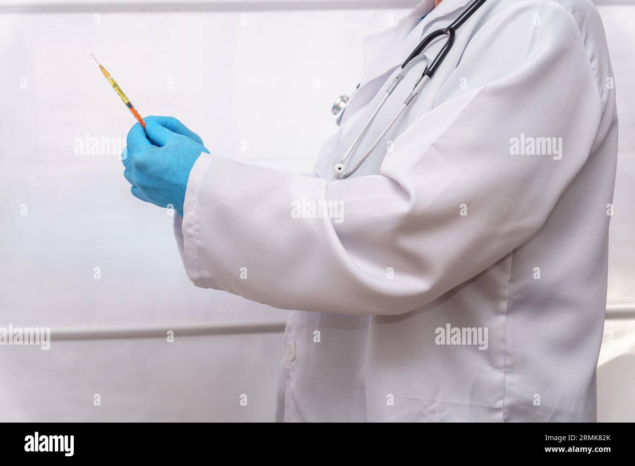 Médecin méconnaissable en gants bleus, manteau blanc et stéthoscope avec une seringue dans sa main Banque D'Images