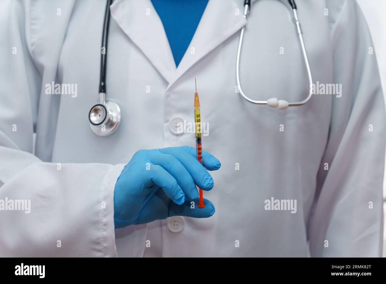 Médecin méconnaissable en gants bleus, manteau blanc et stéthoscope avec une seringue dans sa main Banque D'Images