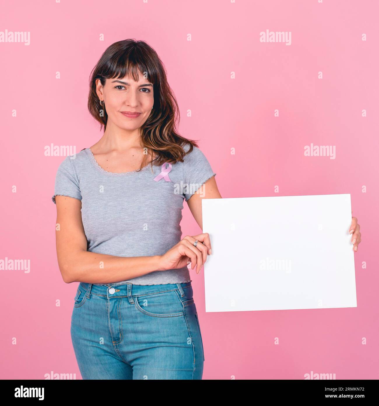 Une femme portant un ruban rose de sensibilisation au cancer du sein tenant un panneau blanc sur un fond rose Banque D'Images