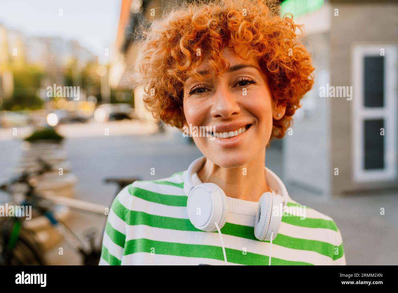 Ginger femme d'âge moyen debout dehors avec un casque sur le cou et souriant à l'appareil photo Banque D'Images