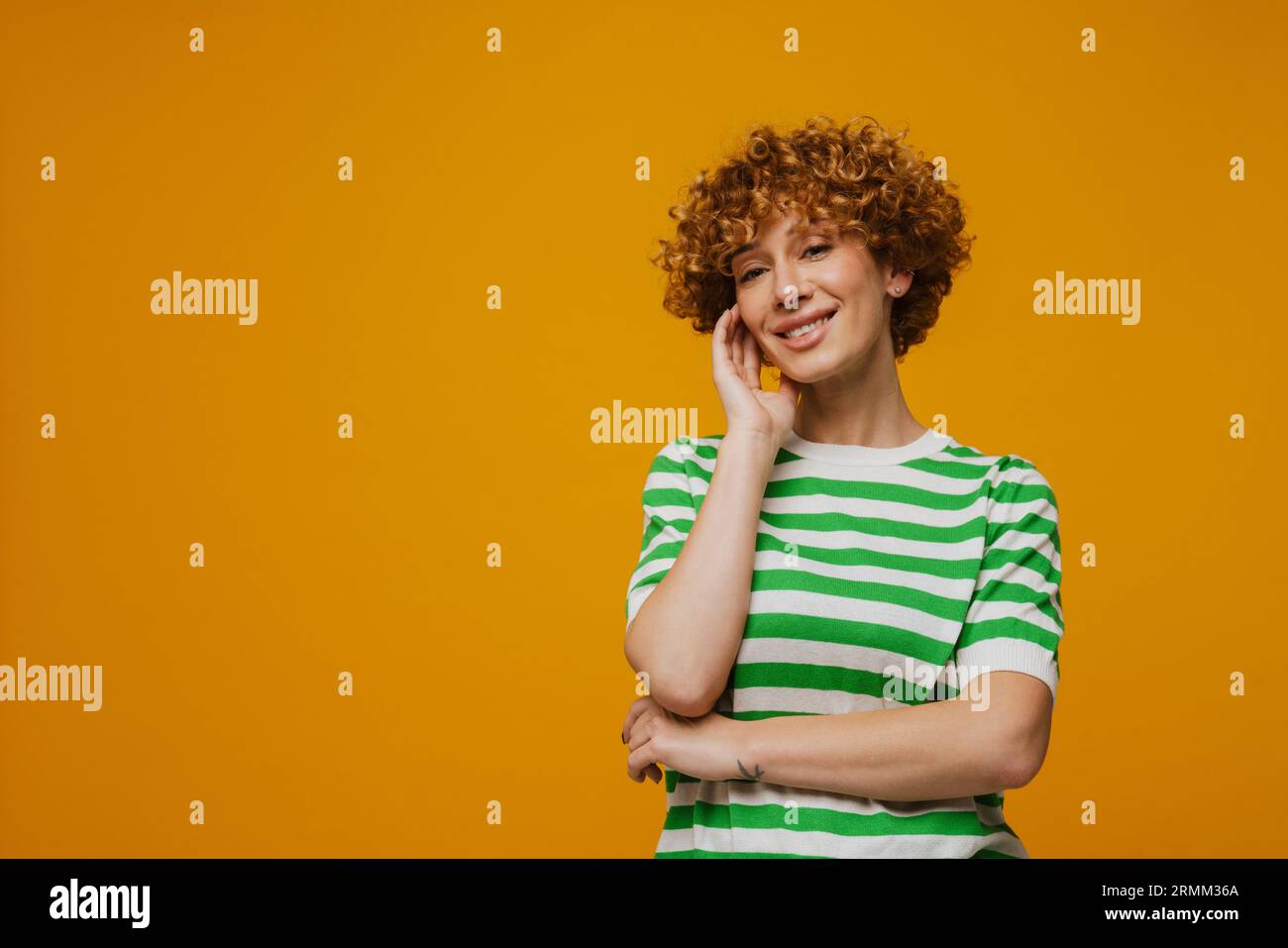 Femme gingembre en t-shirt rayé souriant et regardant la caméra isolée sur fond jaune Banque D'Images
