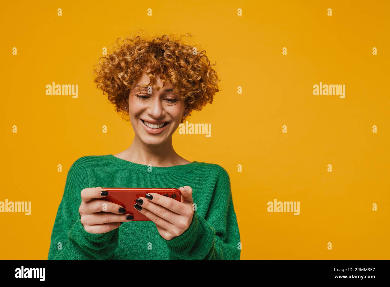 Femme gingembre d'âge moyen jouant au jeu en ligne sur smartphone sur fond jaune Banque D'Images