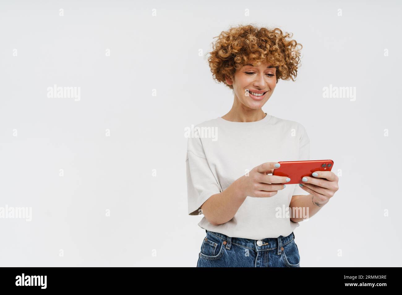 Femme mature joyeuse jouant au jeu en ligne sur téléphone portable isolé sur fond de studio blanc Banque D'Images