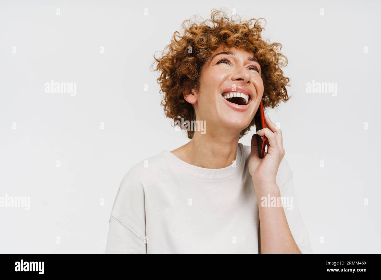 Femme frisée de gingembre riant et parlant sur téléphone portable isolé sur fond blanc Banque D'Images