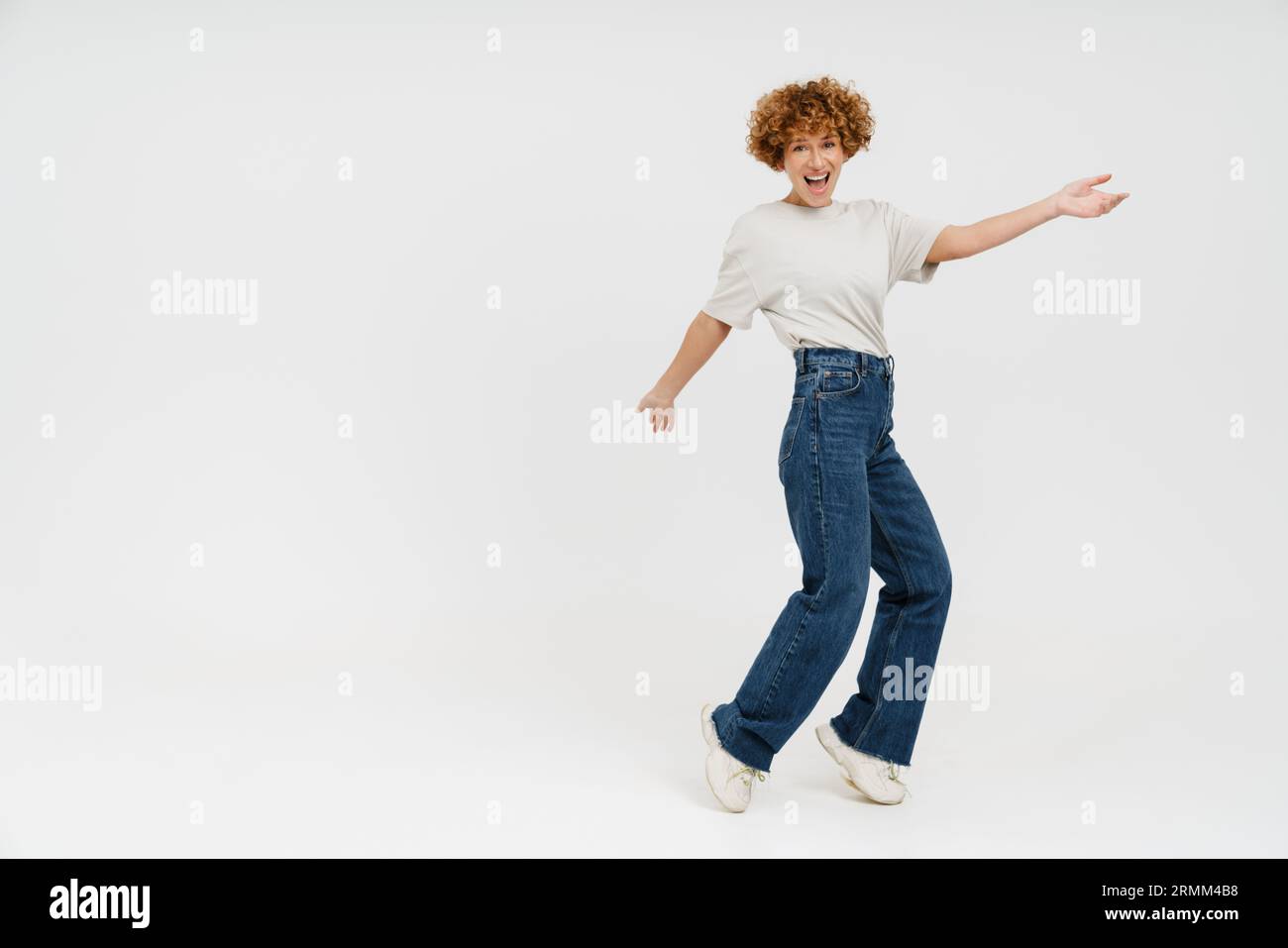 Femme bouclé de gingembre portant un t-shirt souriant et dansant isolé sur fond blanc Banque D'Images