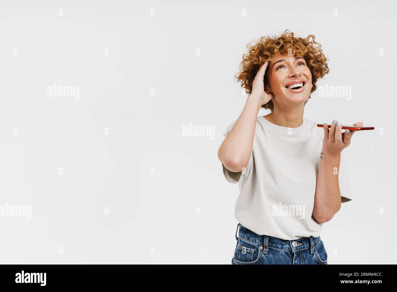 Femme bouclé de gingembre portant un t-shirt souriant et parlant sur téléphone portable isolé sur fond blanc Banque D'Images