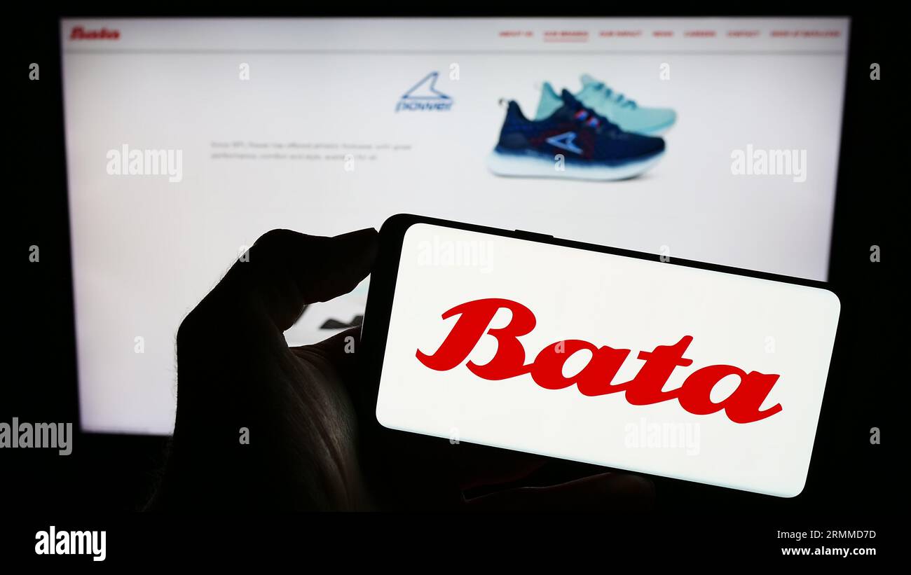 Personne tenant le téléphone portable avec le logo de la compagnie de chaussures Bata Corporation sur l'écran en face de la page Web d'affaires. Concentrez-vous sur l'affichage du téléphone. Banque D'Images