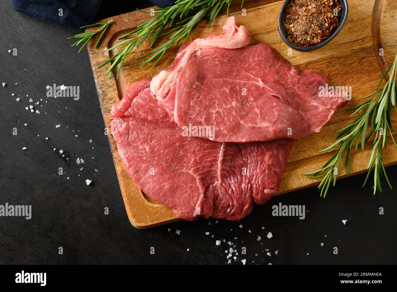 Steak de ribeye marbré cru avec branche de romarin sur fond noir. Espace de copie. Vue d'en haut. Gros plan. Banque D'Images