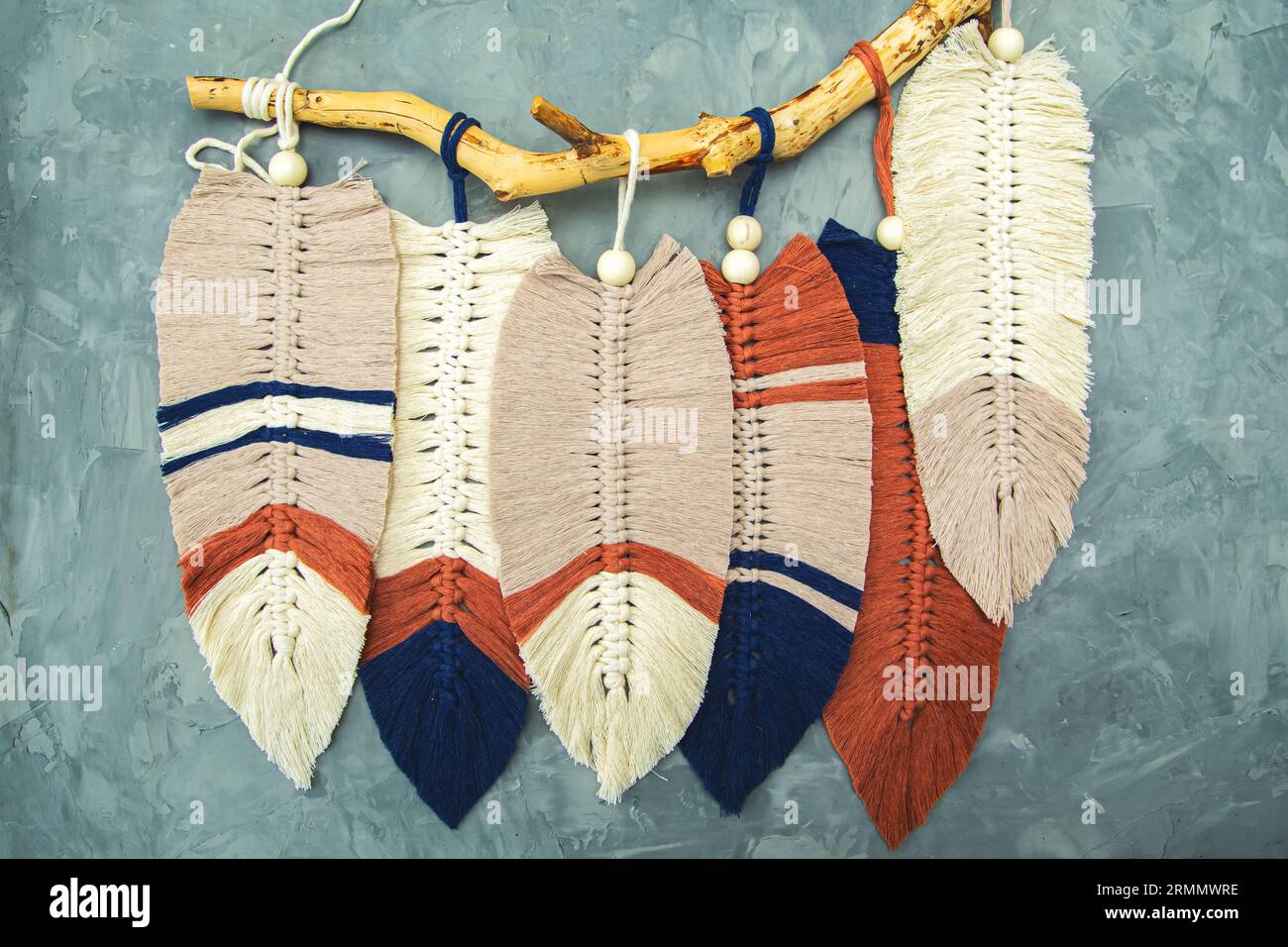 Panneau mural dans le style Boho fait de cordons de coton beige, bleu et rouge en utilisant la technique macramé. Décoration moderne tendance, atmosphère chaleureuse, fond gris. Banque D'Images