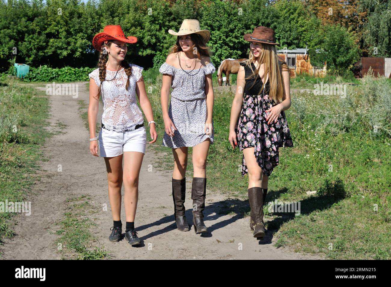 trois jeunes cow-girls marchant à la vieille ferme dans la journée ensoleillée d'été Banque D'Images
