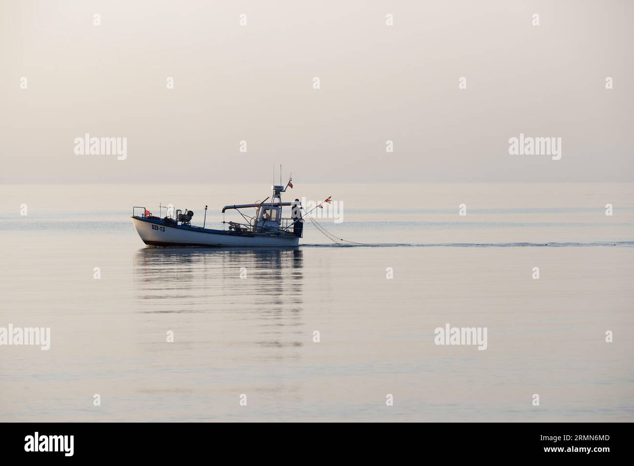 Petit bateau de pêche commercial se dirigeant vers la mer calme, fond lumineux ( Dziwnów ) Banque D'Images