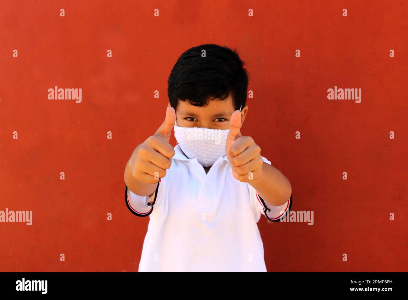 Joyeux et pensif Latino garçon de 8 ans portant une chemise blanche d'uniforme scolaire et un masque facial pour la protection contre la pandémie de Covid-19 à la rentrée scolaire Banque D'Images