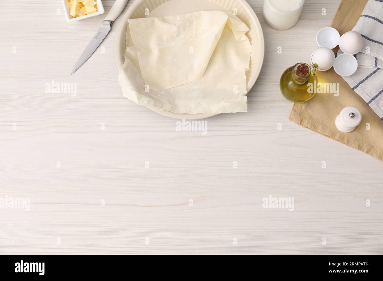 Pâte fraîche et différents ingrédients pour faire du baklava sur table en bois blanc, pose à plat. Espace pour le texte Banque D'Images