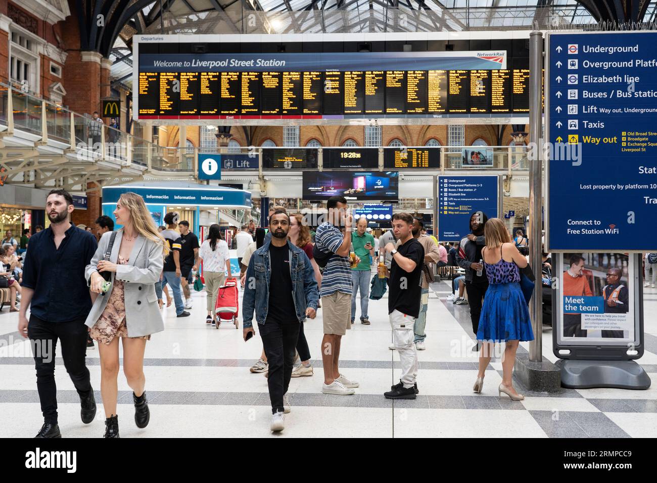 Les passagers ferroviaires marchant à travers la gare de Liverpool Street avec un panneau de bienvenue et les heures de départ du train panneau électronique derrière. Londres, Angleterre Banque D'Images