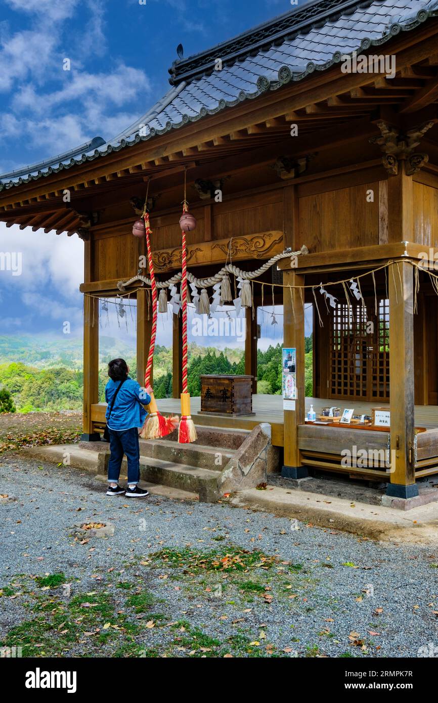 Japon, Kyushu. Sanctuaire shinto sur le terrain du château d'Oka, préfecture d'Oita. Femme sonnant Bell pour annoncer sa présence à la Déité dans le Sanctuaire. Banque D'Images