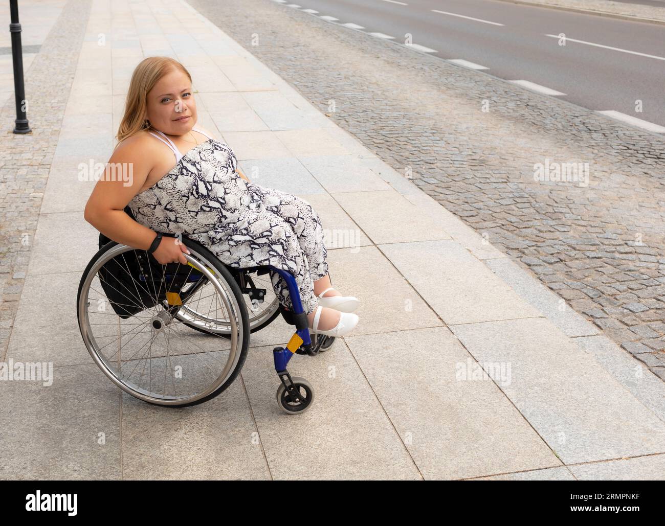 Souriant Jeune jolie femme avec petite stature sur les stands de fauteuil roulant sur l'arrêt de bus extérieur en attente des transports publics le jour de l'été. Femelle adulte avec Banque D'Images