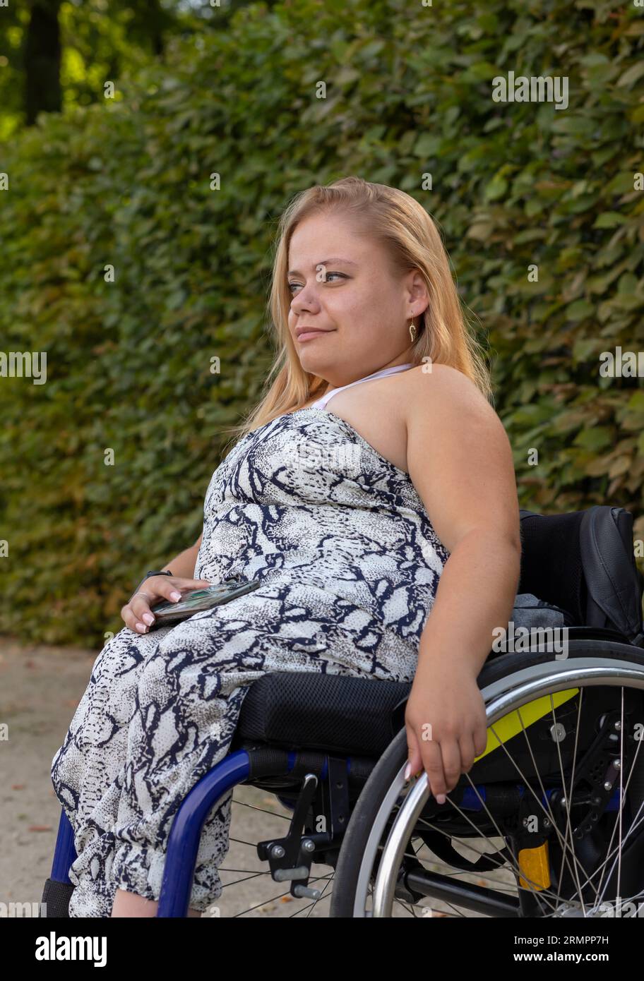 Young Pretty Woman with Short Height on Wheelchair profite du temps à Green Park le jour de l'été. Souriant Femme adulte avec handicap. Plan vertical Banque D'Images