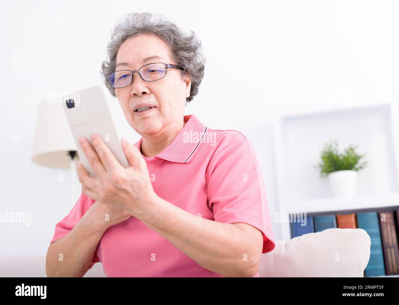 Femme âgée assise sur le canapé et naviguant sur le téléphone portable Banque D'Images