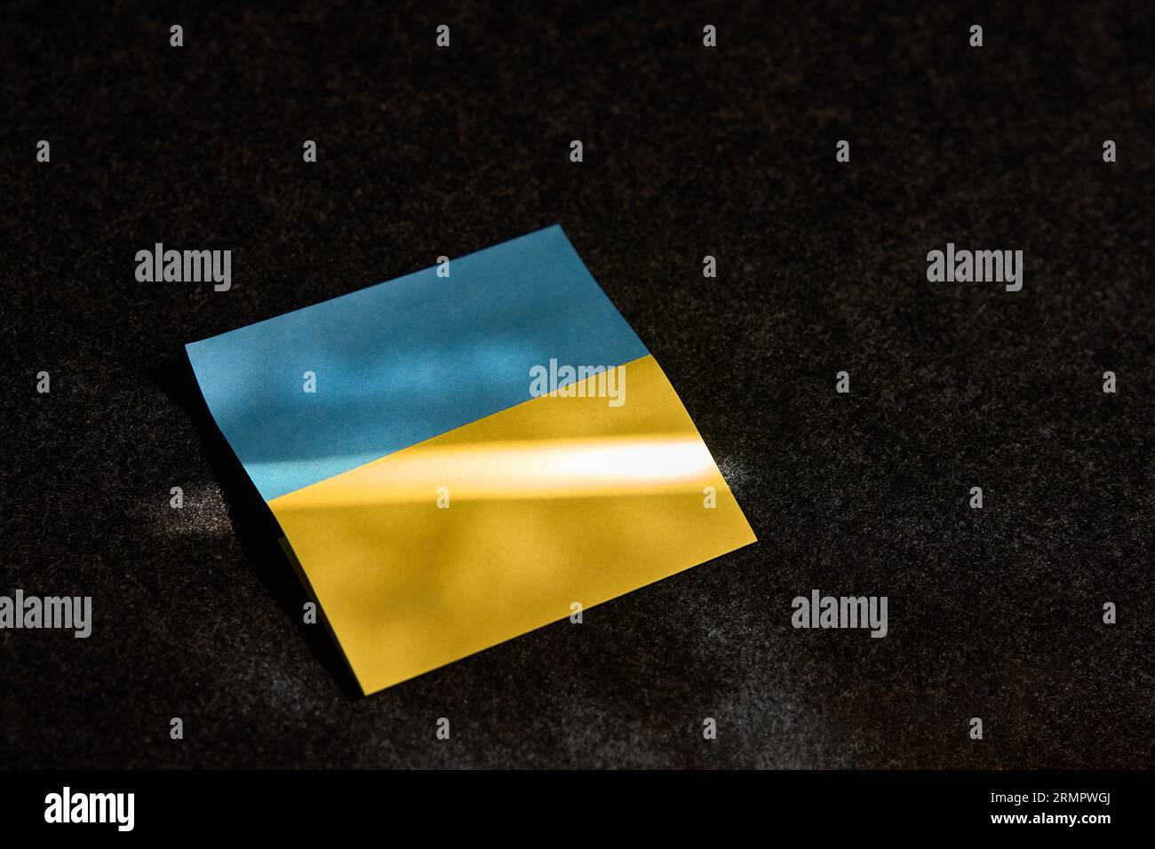 L'autocollant sous la forme du drapeau ukrainien se trouve. sur une surface sombre et un rayon de soleil tombe dessus Banque D'Images