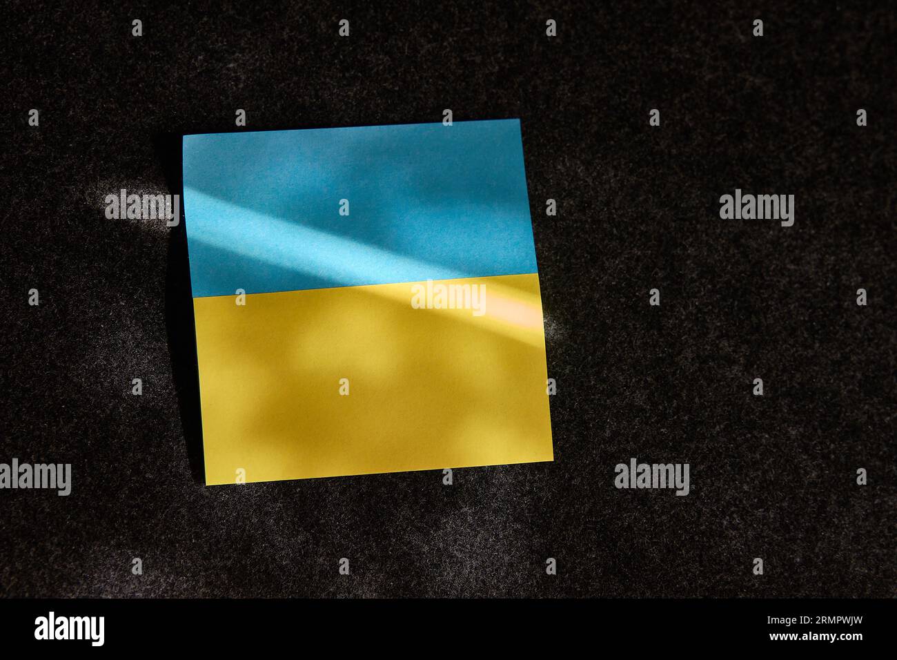 L'autocollant sous la forme du drapeau ukrainien se trouve. sur une surface sombre et un rayon de soleil tombe dessus Banque D'Images