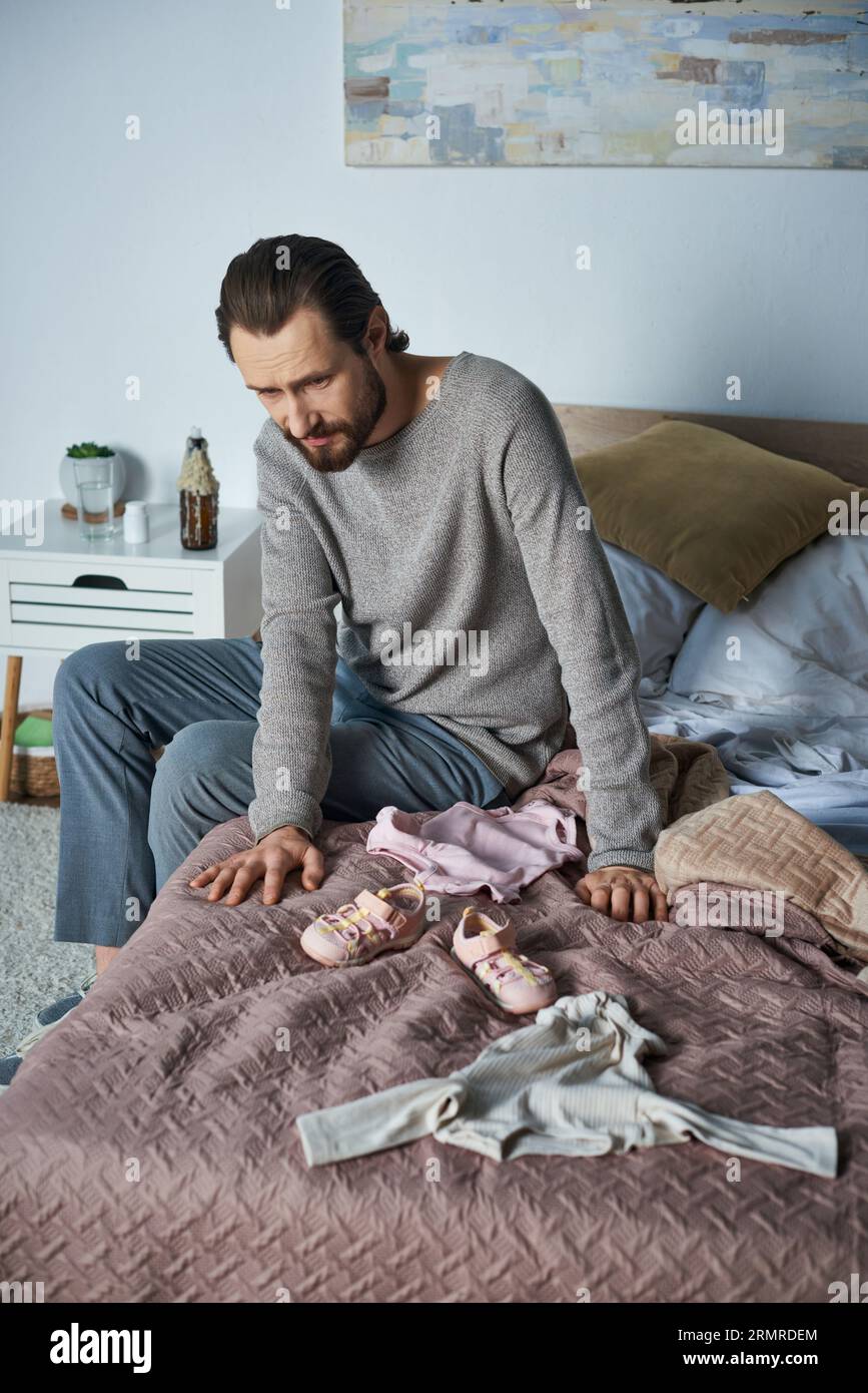 chagrin, homme déprimé pleurant près des vêtements de bébé, assis sur le lit, concept de fausse couche, chagrin Banque D'Images