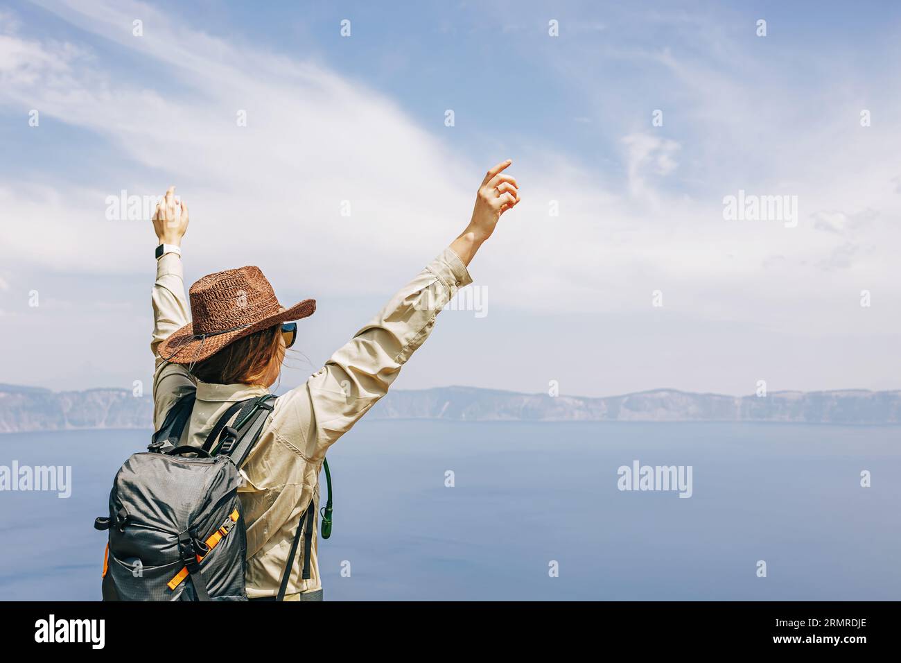 Femme dans un chapeau debout avec ses mains levées avec une vue sur un lac, voyage d'été Banque D'Images