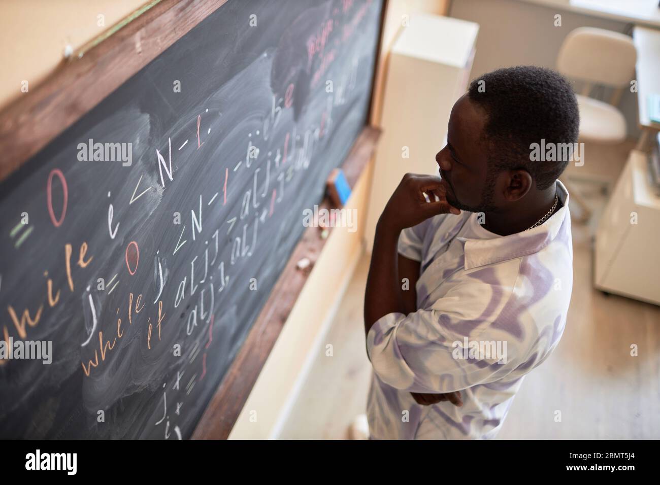 Pensif afro-américain étudiant ou enseignant debout devant le tableau noir avec des formules écrites et des équations dans la salle de classe Banque D'Images