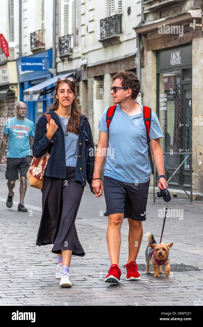 Jeune couple marchant dans le centre-ville main dans la main avec un petit chien terrier - Tours, Indre-et-Loire (37), France. Banque D'Images