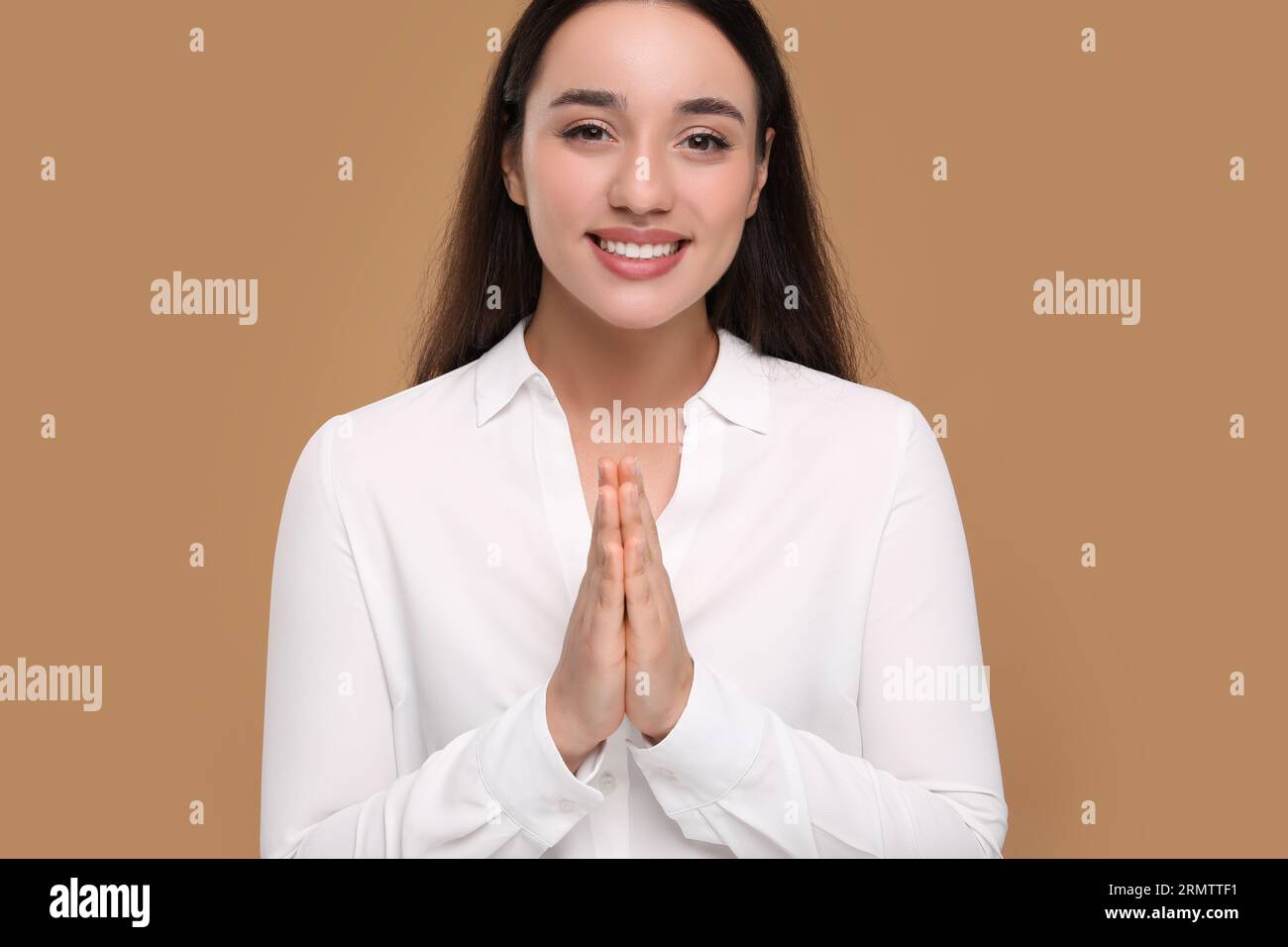 Merci geste. Belle femme reconnaissante avec les mains serrées ensemble sur fond brun Banque D'Images