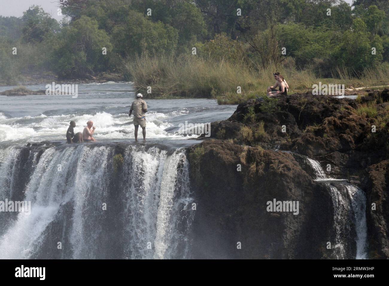 (141002) -- CHUTES VICTORIA, -- des touristes étrangers posent pour des photos avec des guides locaux à la piscine du diable au sommet des chutes Victoria, aux frontières du Zimbabwe et de la Zambie, 30 septembre 2014. La piscine du diable est un site majeur pour les touristes aux chutes Victoria pendant la saison sèche, en particulier pour les mois de septembre et octobre où les niveaux d'eau sont au plus bas et le courant du fleuve Zambèze est doux. Protégée uniquement par les instructions des guides locaux, la baignade dans la piscine, située au bord des chutes Victoria de 108 mètres de haut, a été décrite comme l'une des touris les plus excitantes Banque D'Images