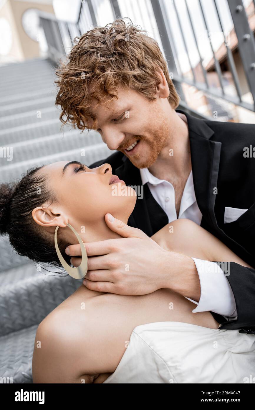 romance urbaine, mariage, tendresse, heureux marié roux embrassant élégante mariée afro-américaine Banque D'Images