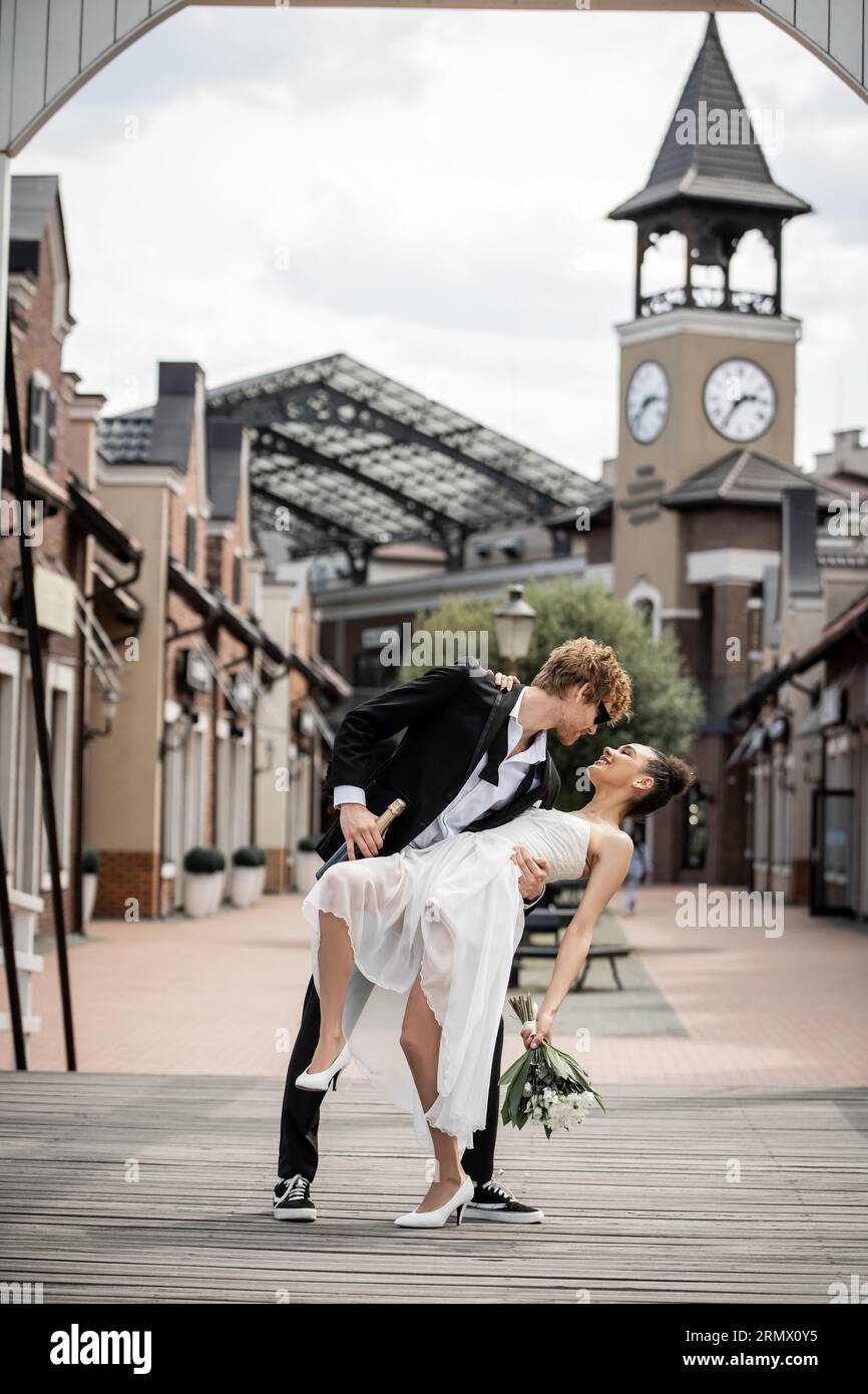 cérémonie de mariage dans la ville européenne moderne, jeune homme embrassant heureuse mariée afro-américaine dans la rue Banque D'Images