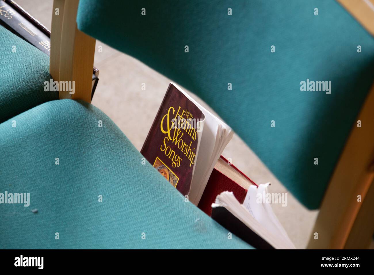 Un livre d'hymnes et de chants d'adoration sous une chaise à l'intérieur d'une église Banque D'Images
