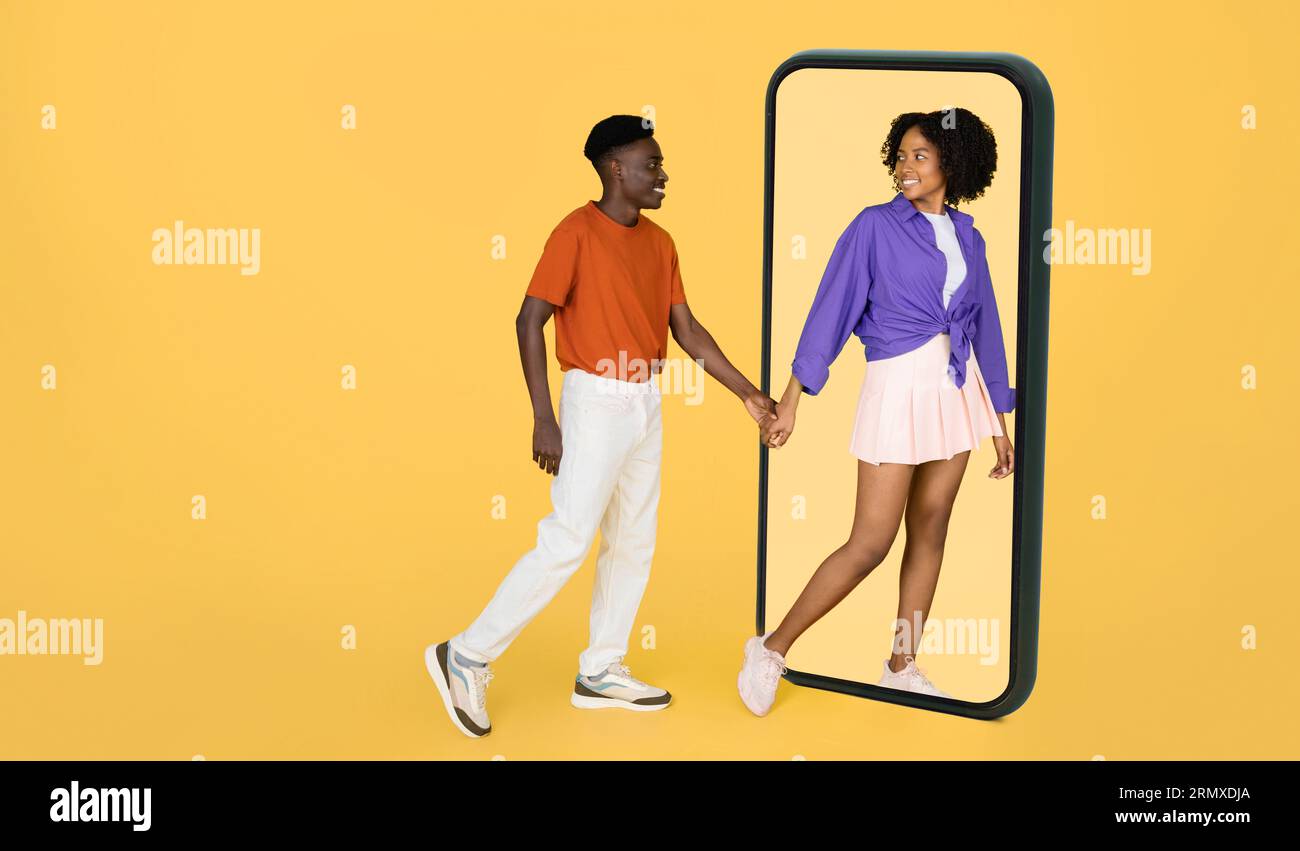 Positive Millennial femme noire dans la main de l'homme de tenir casual, mène à grand smartphone, profiter de la date et du temps libre Banque D'Images