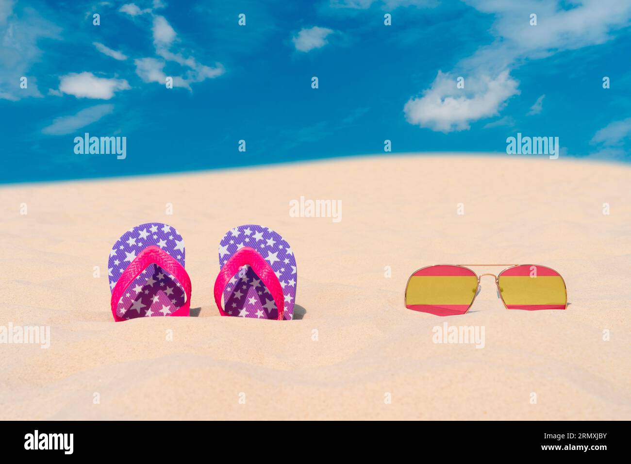 Lunettes de soleil avec des lunettes en forme de drapeau de l'Espagne et tongs reposent sur le sable contre le ciel bleu. Concept de vacances d'été et de voyage en Espagne Banque D'Images