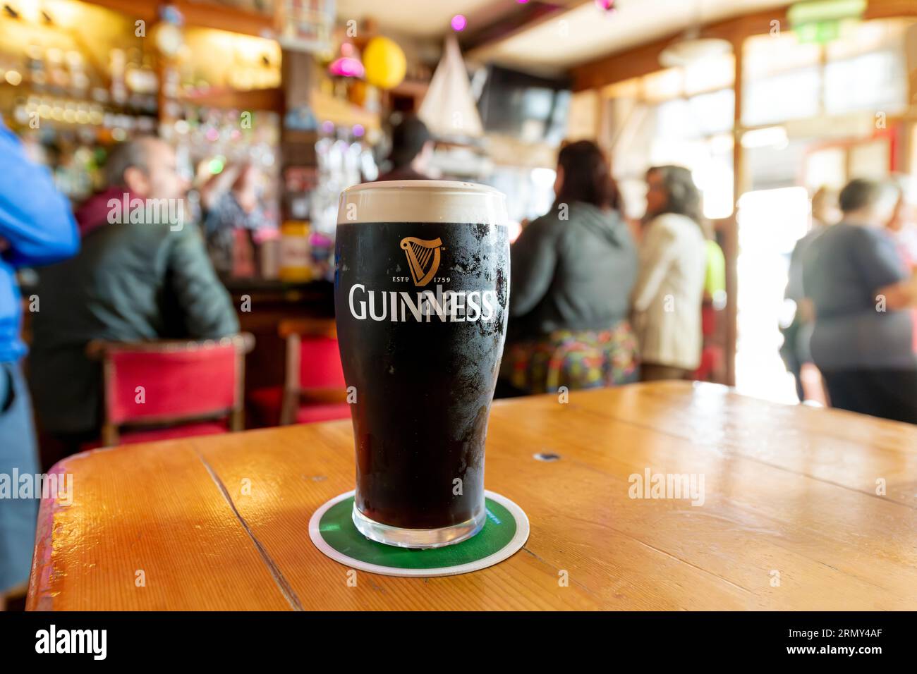 Vue générale d'une pinte complète de Guinness Irish Dry stout Beer dans un pub animé coloré dans la ville de Cobh, Irlande. Banque D'Images