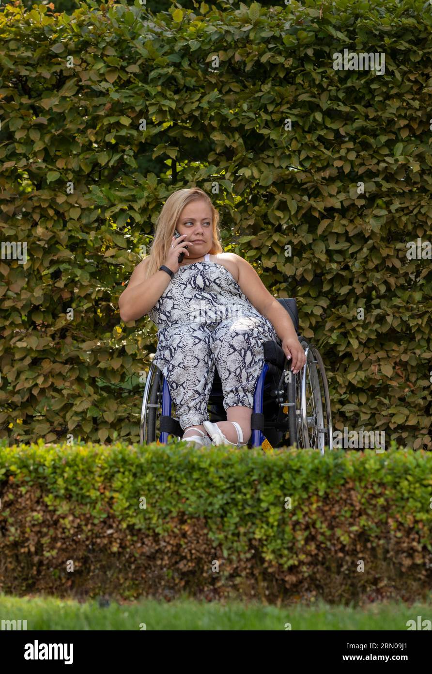 Pleine longueur jeune femme en fauteuil roulant parle au téléphone à Green Park le jour de l'été. Adulte handicapé féminin occupé. Plan vertical Banque D'Images