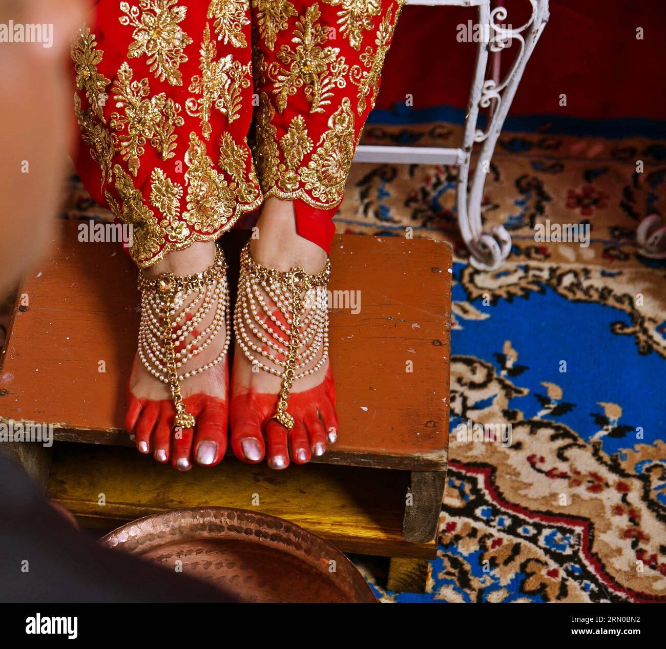 Cérémonie de mariage coutumier népalais les pieds de la mariée ornés de motifs complexes de henné et ornés de ongles d'orteil avec sarée rouge et tapis bleu. Banque D'Images